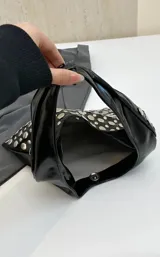 Cartera tipo hobo de color negro con acabado brillante, decorada completamente con remaches metálicos circulares de diversos tamaños.