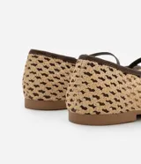 Zapatilla tipo bailarina con capellada tejida con efecto rafia color beige, punta redonda, tira fina marrón con hebilla y suela marrón.