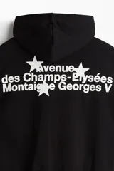 Campera con capucha negra, de corte holgado (boxy), con cierre bidireccional y bolsillos canguro delanteros.