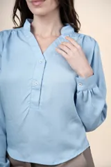 Blusa celeste de tencel con cuello mao, escote en V con botones frontales y mangas largas con puños ajustados.