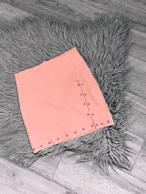 Minifalda color salmón con hilera de tachas plateadas en el lateral.