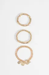 Set de tres pulseras doradas con diferentes diseños: una de tubos metálicos, una de cuentas esféricas con un segmento central liso y una de cadena de eslabones con cierre de barra y dijes colgantes.