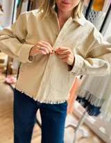 Campera color beige de gabardina con corte clásico, cierre frontal con botones y ruedo con flecos.