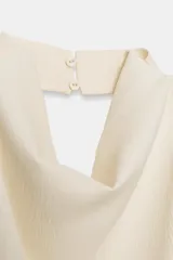 Top color crema confeccionado en viscosa, con cuello halter drapeado, espalda descubierta y bajo asimétrico. Cierre en el cuello con botón.