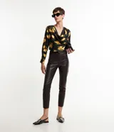 Pantalón skinny de cuero sintético color marrón oscuro, con cierre y botón en la cintura, bolsillos delanteros y traseros, y recortes en las rodillas.