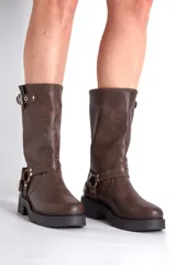 Borcego de cuero color marrón con apliques plateados, caña alta y suela track.