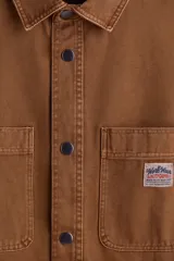 Sobrecamisa de lona gruesa de algodón color marrón, con cuello, tapeta de botones a presión y canesú en la espalda. Mangas largas con botón a presión en los puños y dos bolsillos superiores de parche. Bajo levemente redondeado. Corte oversized.