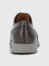 Zapato tipo Oxford estilo brogue con detalles perforados en la puntera y laterales. Presenta capellada de cuero en tono marrón oscuro, cordones al tono y suela de goma gris con diseño deportivo.