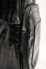 Mochila negra con textura símil cuero de cocodrilo, con dos compartimentos principales con cierre y asa de mano en la parte superior.