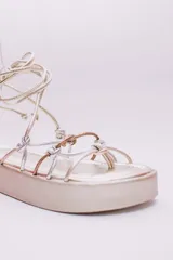 Sandalias negras de ecocuero con plataforma plana y tiras finas que se atan alrededor del tobillo.