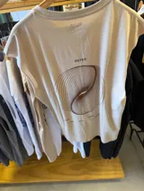 Musculosa color beige claro con estampa gráfica abstracta en marrón, que incluye el texto "OSTEN" y palabras como "STEADY", "DEEP", "BOLD", "ENERGY" y "BALANCE".