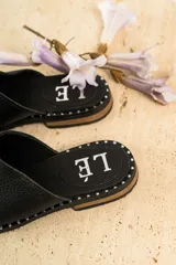 Mules de cuero negro con tachas plateadas en el borde de la suela y plantilla con logo estampado.
