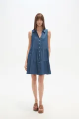 Vestido corto de denim sin mangas, con cuello camisero, cierre frontal con botones y diseño de falda con volados.