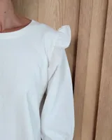 Remera blanca de algodón con cuello redondo, mangas tres cuartos abullonadas y detalle de volados en los hombros.