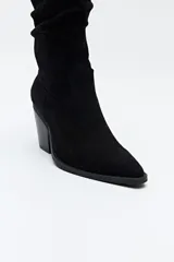 Bota texana de caña alta confeccionada en gamuza negra, con punta fina y taco cuadrado de 5 cm. Presenta un diseño con efecto arrugado en la caña y cierre lateral para facilitar su colocación.