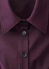 Vestido midi de corte evasé en color violeta oscuro, con cuello camisero, sin mangas y cierre frontal con botones. Incluye un cinturón ajustable a tono que marca la cintura.