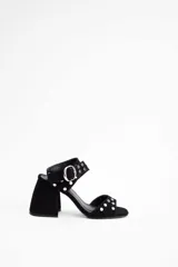 Sandalia de tacón cuadrado color negro, con tiras decoradas con tachas metálicas plateadas y una hebilla grande en el tobillo.