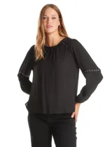 Blusa negra de gasa con cuello a la base fruncido, mangas largas amplias con puños elastizados y apliques de cinta con tachas en la parte delantera y antebrazos. Tiene una abertura central en la espalda con botón.