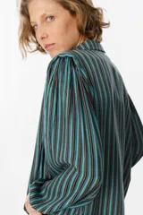 Camisa de manga larga con diseño de rayas verticales en tonos verde, azul y marrón. Presenta cuello clásico, cierre frontal con botones y mangas abullonadas con puños ajustados.