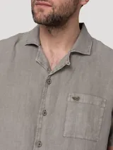 Camisa de manga corta color gris, de corte regular y estilo casual, confeccionada en lino orgánico con cuello sastre y cierre frontal de botones.