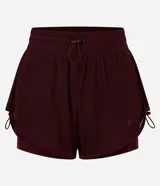 Bermuda deportiva femenina modelo runner, color bordó, con short interno incorporado. Presenta cintura elástica con cordón de ajuste y laterales con cordones ajustables. Confeccionada en tejido de tul con tecnología dry para mayor transpirabilidad.