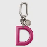 Llavero o charm de letra A en color fucsia, con mosquetón metálico y dije circular pequeño con la marca grabada.