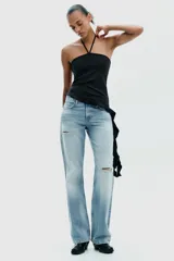 Top negro de cuello halter con lazada, escote recto y hombros descubiertos. Presenta un volante asimétrico en el lateral.