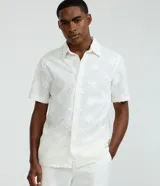 Camisa de manga corta color blanco con diseño bordado de flores, cuello inglés y cierre frontal de botones.