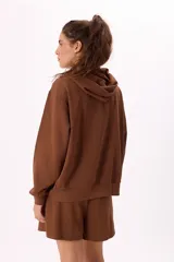 Conjunto deportivo compuesto por un buzo con cierre frontal, capucha y bolsillos, y un short con cintura elástica y cordón ajustable. Confeccionado en tejido soft premium de color marrón.
