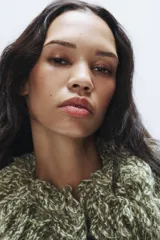 Chaqueta de punto de textura jaspeada en color verde, con cuello redondo adornado con flecos del mismo tejido, manga larga y cierre frontal con corchete metálico.