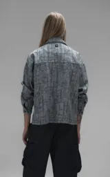 Campera de denim rígido con diseño de trama texturizada en tonos grises y negros. Presenta cuello camisero, cierre frontal con botones, mangas largas y dos bolsillos frontales con solapa.