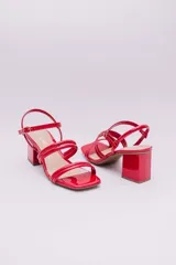 Sandalias de tacón cuadrado medio, confeccionadas en charol rojo. Presentan un diseño de tiras tubulares sobre el empeine y cierre con pulsera ajustable al tobillo mediante hebilla metálica.