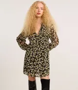 Vestido corto de chiffon negro con estampado de flores blancas y amarillas, escote en V, mangas largas abullonadas y volados en el busto.