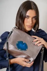 Sobre de cuero metalizado color plateado con solapa frontal decorada con una piedra de ágata azul natural. Incluye correa larga extraíble y cierre trasero.