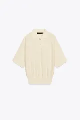 Polo de punto color crema, de manga corta y corte holgado, con cuello polo y tres botones frontales.