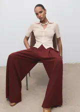 Pantalón de tiro medio color bordó, de diseño wide leg con pinzas delanteras y bolsillos laterales. Cuenta con cierre de cremallera, botón y ganchos ocultos con tapeta, además de forro interior.
