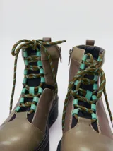 Bota estilo trekking de cuero en tonos marrones y verde oliva, con plataforma de goma, cordones tipo cuerda de escalada con detalles en color turquesa y collar acolchado.