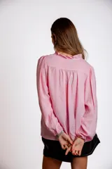 Camisa celeste con cuello con volados y lazos, mangas largas con puños elásticos y corte holgado.