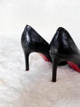 Zapatos de tacón alto con textura de reptil, color negro, con suela roja característica.