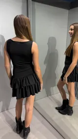 Vestido corto negro sin mangas, con escote redondo y falda con doble volado en el ruedo.