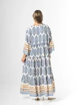 Maxi vestido largo de fibrana en color blanco con estampado paisley y geométrico en tonos azules y tostados, con escote en V, mangas largas amplias y diseño holgado con volados en la falda.