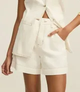 Short de sarga color blanco, tiro alto, corte mom, con botón forrado, bolsillos laterales y costuras contrastantes.