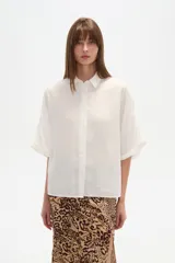 Camisa de viscosa color blanco, de corte holgado, con cuello clásico y cierre frontal de botones. Presenta mangas cortas con diseño amplio.