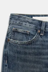 Jeans de tiro medio con corte cropped, confeccionados en denim azul con efecto lavado. Presentan trabillas en la cintura, cierre frontal con cremallera y botón metálico, bolsillos delanteros y traseros, y costuras laterales decorativas.