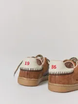 Championes de cuero con diseño tricolor en tonos negro, marrón y crema. Presentan cordones trenzados, costuras a la vista y detalle de pespuntes en el talón.