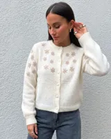 Cardigan de punto color blanco con diseño de flores bordadas en tono beige, cuello redondo, cierre frontal con botones forrados y mangas largas con puños acanalados.