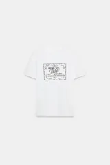 Camiseta blanca de manga corta y cuello redondo, con aplicación de organza y texto negro a contraste en el pecho.