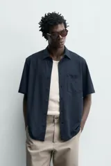 Camisa azul marino de corte regular fit confeccionada en tejido fluido de algodón y lino, con cuello solapa, manga corta, bolsillo aplicado en el pecho y cierre frontal con botones.