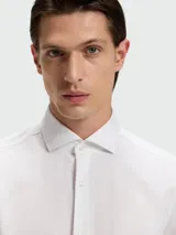 Camisa de vestir blanca de manga larga para hombre, con cuello clásico y puños franceses (se aprecian gemelos). Corte ajustado al cuerpo.