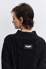 Sweater de punto con diseño de trenzas, cuello alto y mangas largas con puños acampanados. Presenta un corte holgado con terminación asimétrica en el ruedo.